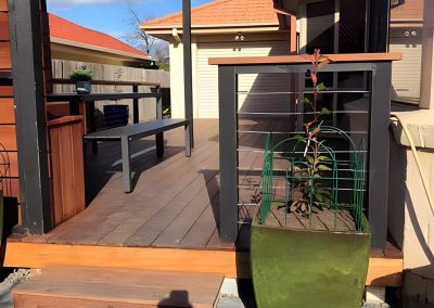 Covered timber deck with steps up from a paved path and a potted plant at the entry