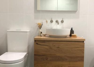 Wall-hung timber vanity with vessel basin beside a toilet on black floor tiles
