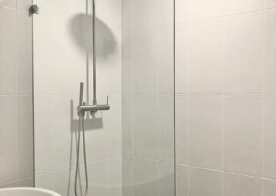 Frameless shower with round rain shower head and dark floor tiles beside a freestanding bath