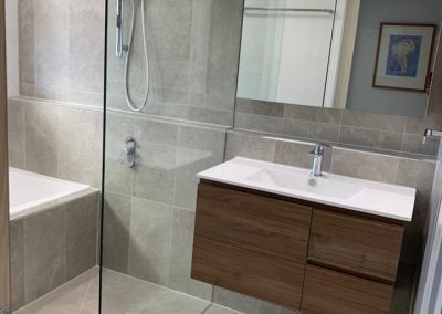 Frameless shower screen, timber vanity and built-in bath in a grey-tiled bathroom