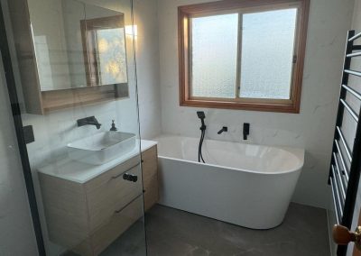Bathroom with back-to-wall bath, timber vanity and black heated towel ladder