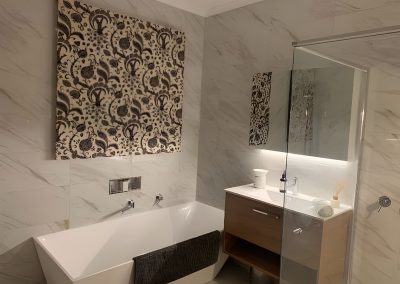 Freestanding bath, timber vanity and patterned wall art on marble-look tiles