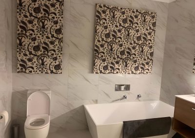 Freestanding bath and toilet below two patterned wall panels on marble-look tiles