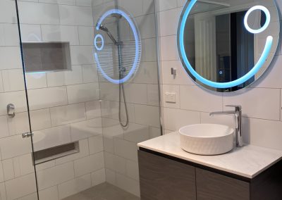 Frameless shower with an LED-lit round mirror and dark wall-hung vanity