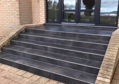 Dark tiled steps up to a glass front entry, close view