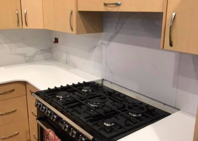 Corner of a kitchen with a black gas cooker, white benchtop and marble-look splashback