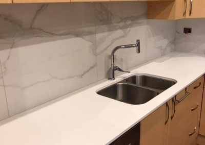 Kitchen sink in a white stone benchtop with marble-look splashback and dark dishwasher