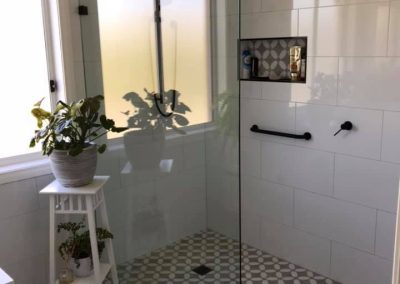 Walk-in shower with patterned floor tiles, black grab rail and patterned niche