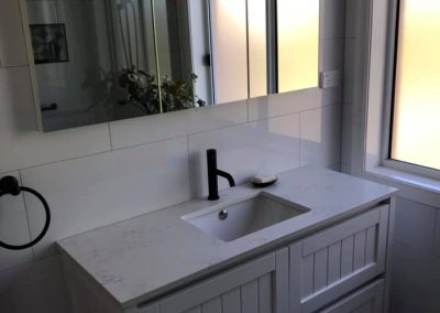 White vanity with black tapware, wide mirror cabinet and patterned floor tiles