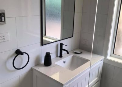 White vanity with an arched black-framed mirror, black tapware and towel ring