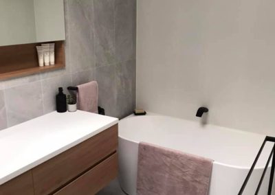 Back-to-wall bath and wall-hung timber vanity in a grey-tiled bathroom