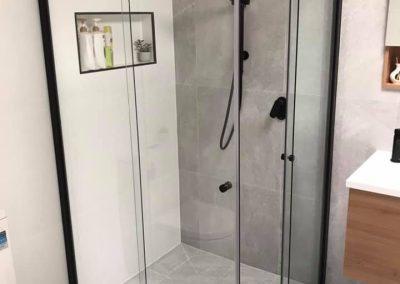 Black-framed sliding shower screen with a recessed niche and black rail shower