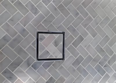 Herringbone marble-look floor tiles around a square tile-insert floor waste