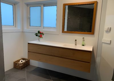 Wall-hung timber vanity under a timber-framed mirror beside frosted windows