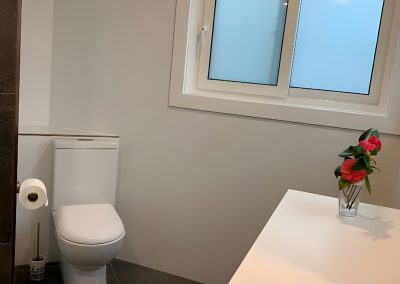 Toilet in a bathroom with large dark floor tiles and a frosted window