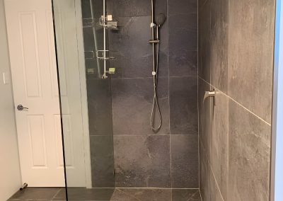 Walk-in shower with a frameless glass panel and large grey tiles