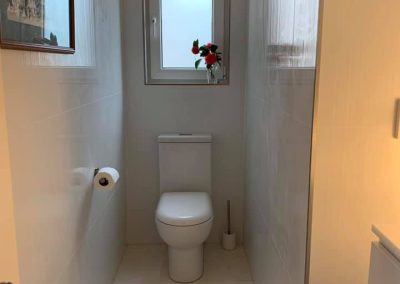 Narrow toilet room with polished floor tiles and a small window