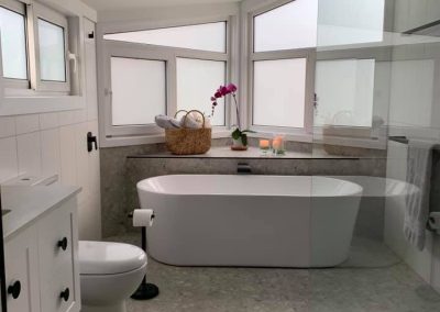 Wide view of a bathroom with freestanding bath, toilet and vanity under corner windows