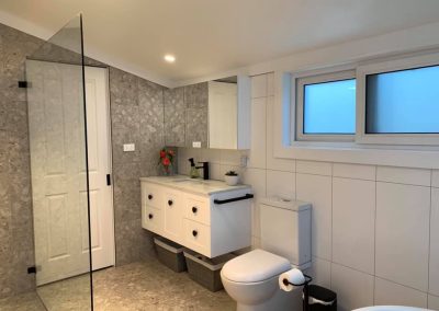 Bathroom with frameless shower panel, white vanity, toilet and terrazzo-look feature tiles