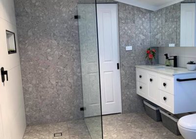 Walk-in shower with frameless panel, black rain shower and terrazzo-look tiles