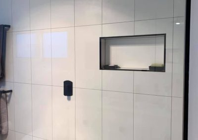 Shower wall with large white tiles, black rain shower head and recessed niche