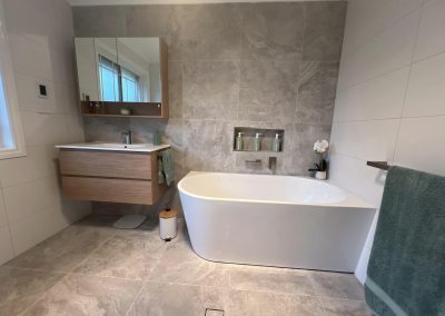 Back-to-wall bath and wall-hung timber vanity with grey feature tiles and a niche