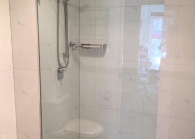Frameless glass shower with chrome rail shower and white marble-look tiles