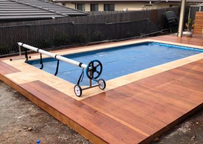 Timber deck around an in-ground pool with a pool cover roller