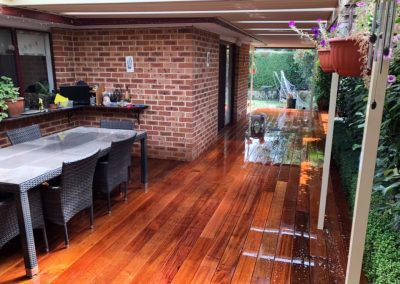 Covered timber deck with an outdoor dining setting beside a brick house
