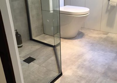 Black-framed shower screen and wall-hung toilet in a bathroom with grey floor tiles