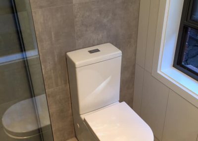 Toilet beside a black-framed shower screen with large grey wall tiles