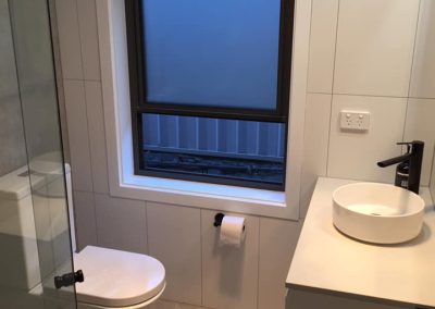 Toilet and white vanity with round basin under a frosted window