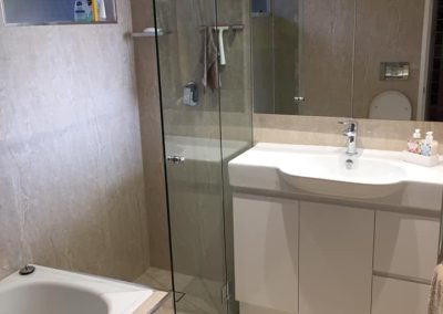 Bathroom with built-in bath, frameless shower screen and white vanity on beige tiles