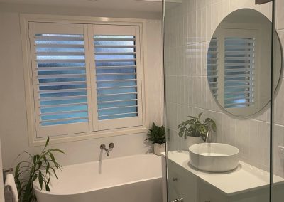 Bathroom with freestanding bath under a shuttered window, vessel basin and round mirror