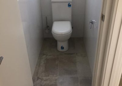 Narrow toilet room with grey floor tiles and a small high window