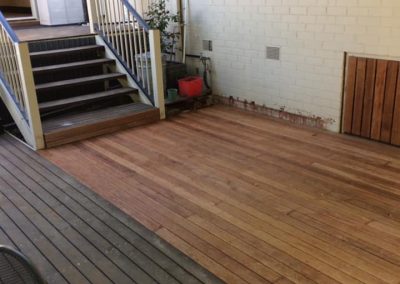 Timber deck being re-laid, new boards beside old weathered boards, with steps up to the house