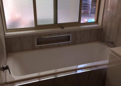 Built-in bath under a frosted window with a marble-look tiled front