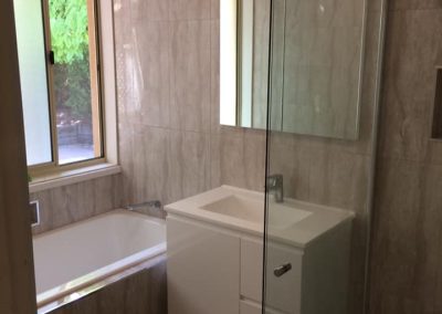Bathroom with built-in bath, white wall-hung vanity and frameless shower on marble-look tiles
