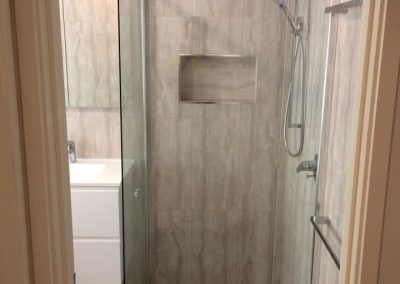 Framed glass shower with recessed niche in a marble-look tiled bathroom