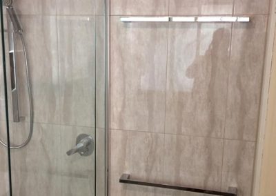 Framed shower door with rail shower and glass shelf on marble-look tiles