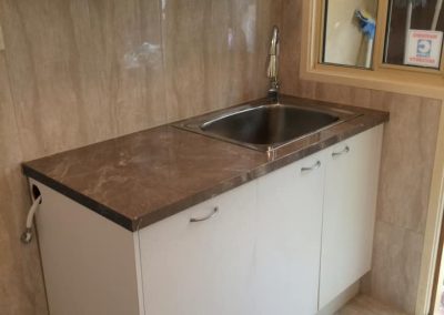 Laundry with white cabinets, stainless steel trough and dark benchtop