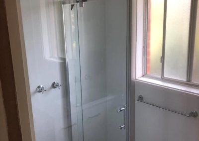 Framed glass shower beside a frosted window with chrome towel rail