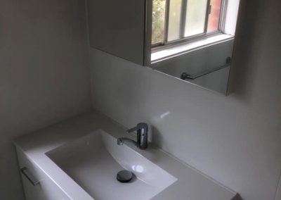 White vanity with integrated basin and chrome mixer below a mirror cabinet