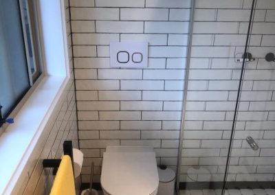 In-wall toilet with white subway tiles and black and white mosaic floor tiles