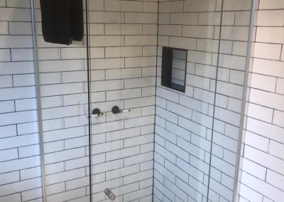Frameless shower with white subway tiles, black niche and black and white mosaic floor