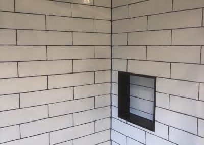 Shower corner with white subway tiles, black rain shower head and black niche