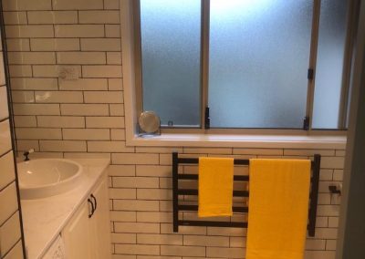 Black heated towel rail with yellow towels under a frosted window, mosaic floor tiles