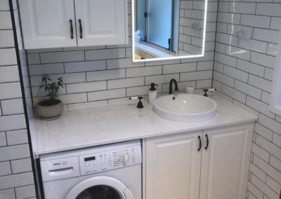 White vanity with round basin over a front-loading washing machine, LED mirror above