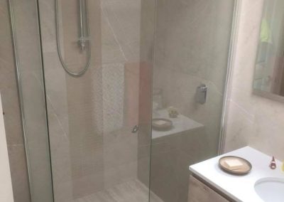 Corner shower with framed glass screen and rail shower beside a timber-look vanity
