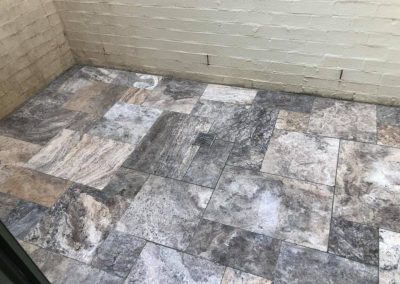 Stone-look floor tiles laid in a pattern against a painted brick wall
